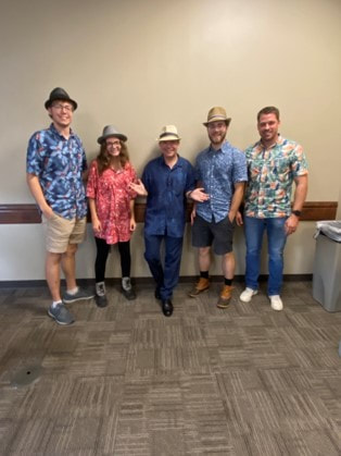 Picture: Dr. Brewer stands with 4 students who prank him by dressing up in Hawaiian shirts & fedoras for class.